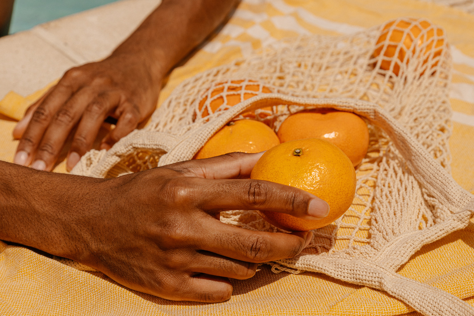 Hand Touching Oranges in Mesh Bag